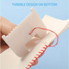 A hand holds a pink sewing guide template with a thimble design on the bottom, showing a needle and red thread.