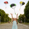 A young girl is joyfully holding a parachute with colorful fabric, playing outdoors on a paved path.