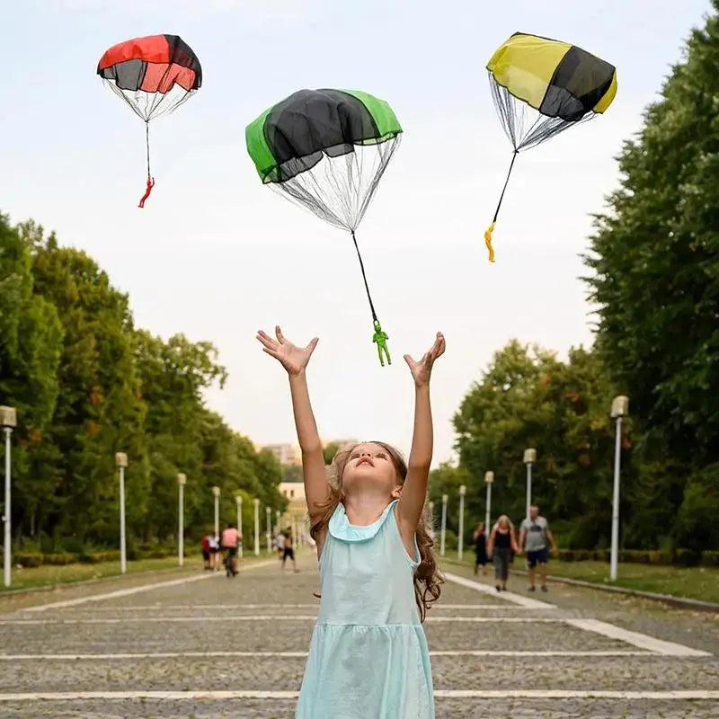 A young girl is joyfully holding a parachute with colorful fabric, playing outdoors on a paved path.
