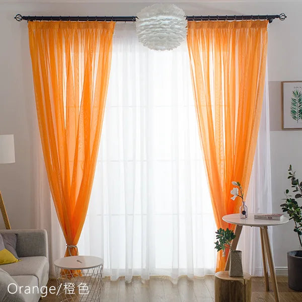 Orange sheer voile curtains with a fluffy spherical light fixture hanging in front of a white window.