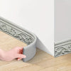 A hand is applying a gray 3D foam wall trim border sticker skirting line to a wooden floor.