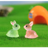 A set of two cute resin miniature bunny figurines, one green and one pink, resting on bright green grass.