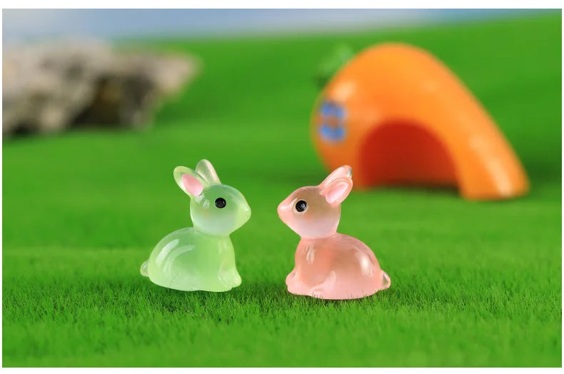A set of two cute resin miniature bunny figurines, one green and one pink, resting on bright green grass.