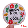 A circular patch featuring embroidered leaves and a red flower with the text BEING NICE IS COOL
