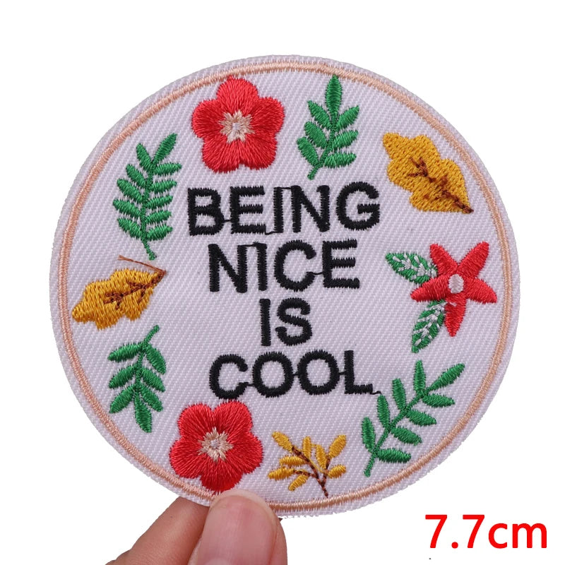 A circular patch featuring embroidered leaves and a red flower with the text BEING NICE IS COOL