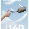 A hand holds a small, dark gray foam inflatable camping pillow against a light blue sky.