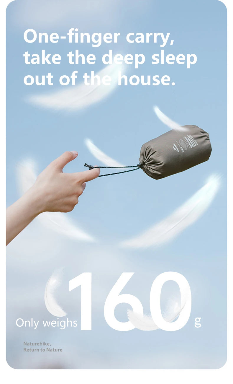A hand holds a small, dark gray foam inflatable camping pillow against a light blue sky.