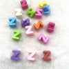 A collection of 10 mixed alphabet letter beads in various colors like pink, purple, blue, and green scattered on white fur.