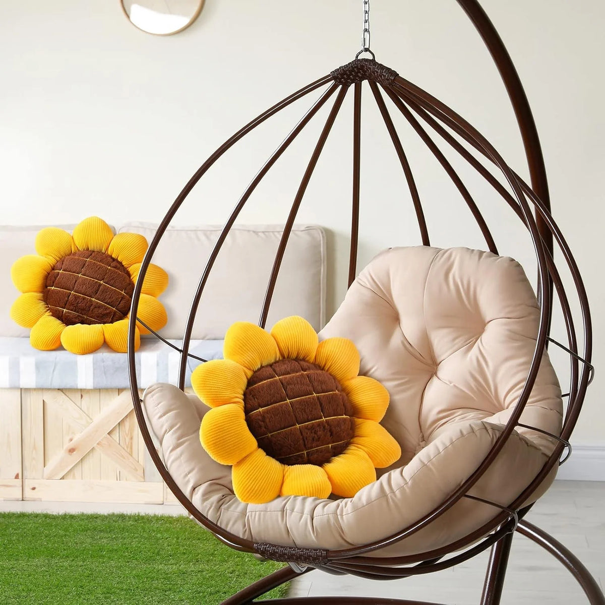 A beige floor pillow shaped like a sunflower is nestled inside a large, dark metal hanging chair.