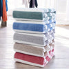 A stack of folded striped microfiber bath towels in shades of blue, gray, and pink on a wooden floor.