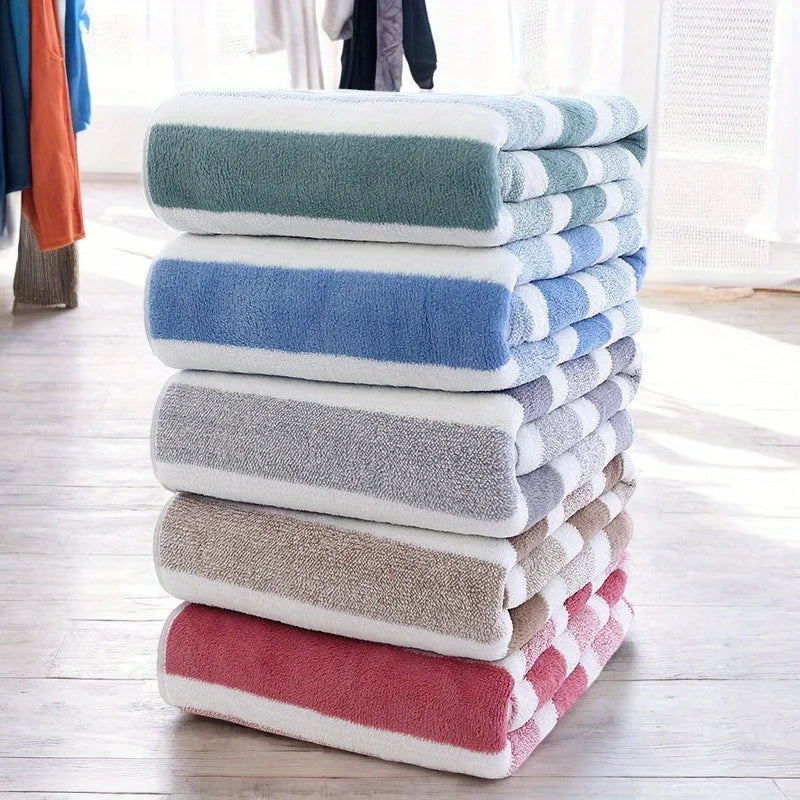 A stack of folded striped microfiber bath towels in shades of blue, gray, and pink on a wooden floor.