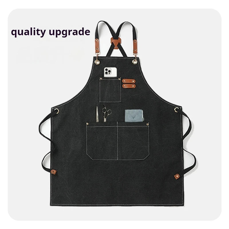 Black chef apron with cross-back straps and tool pockets featuring a smartphone and scissors.