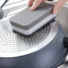 A hand places a gray cleaning sponge onto a silver dish rack for washing.