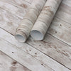 Rolls of retro wood grain self-adhesive wallpaper lying on a weathered white wooden surface.