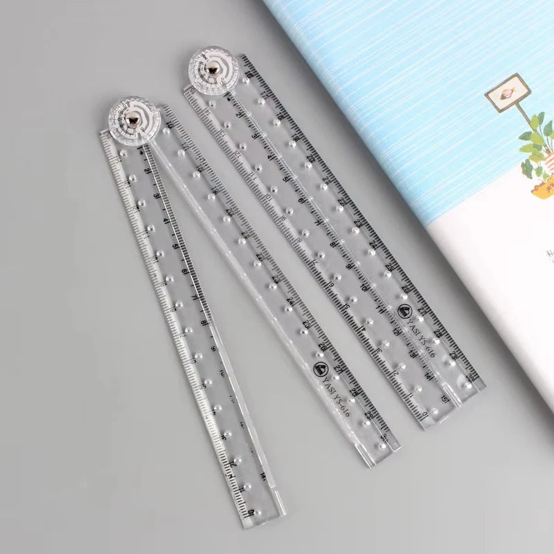 Transparent foldable plastic ruler with a decorative top, shown next to a notebook.
