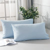 A set of two light blue microfiber pillowcases resting on a white surface with greenery in the background.