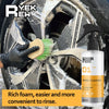 A hand is cleaning a car wheel with a yellow brush and a spray bottle of wheel cleaner foam.