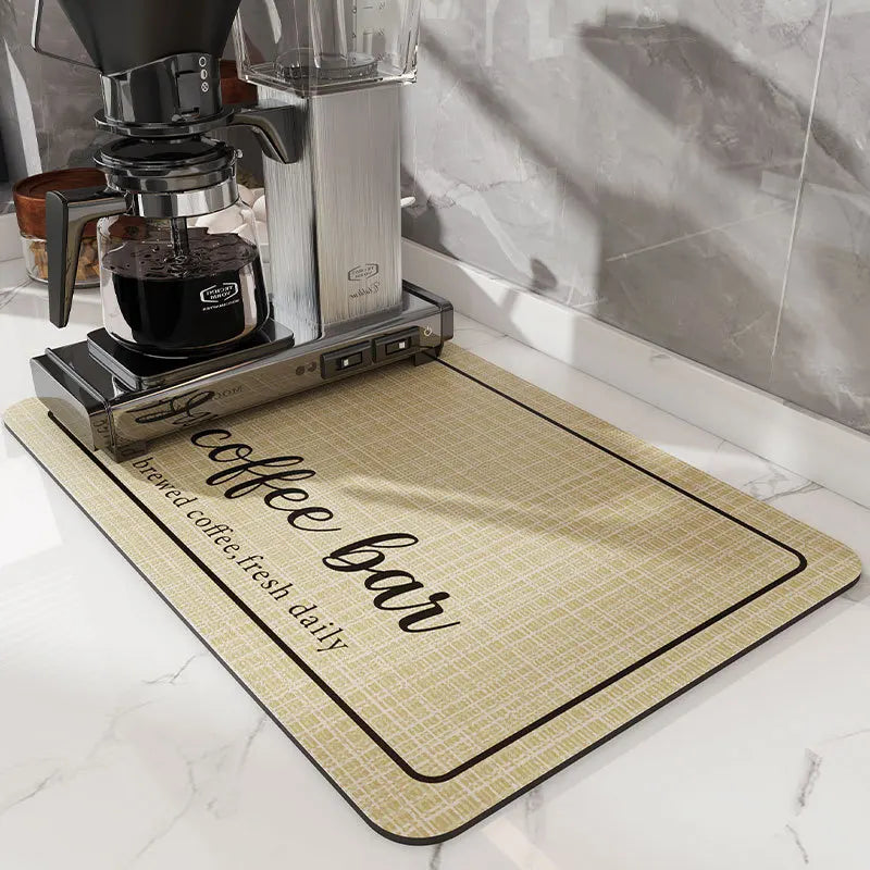 A black coffee grinder sits on a beige mat labeled coffee bar on a white marble countertop.