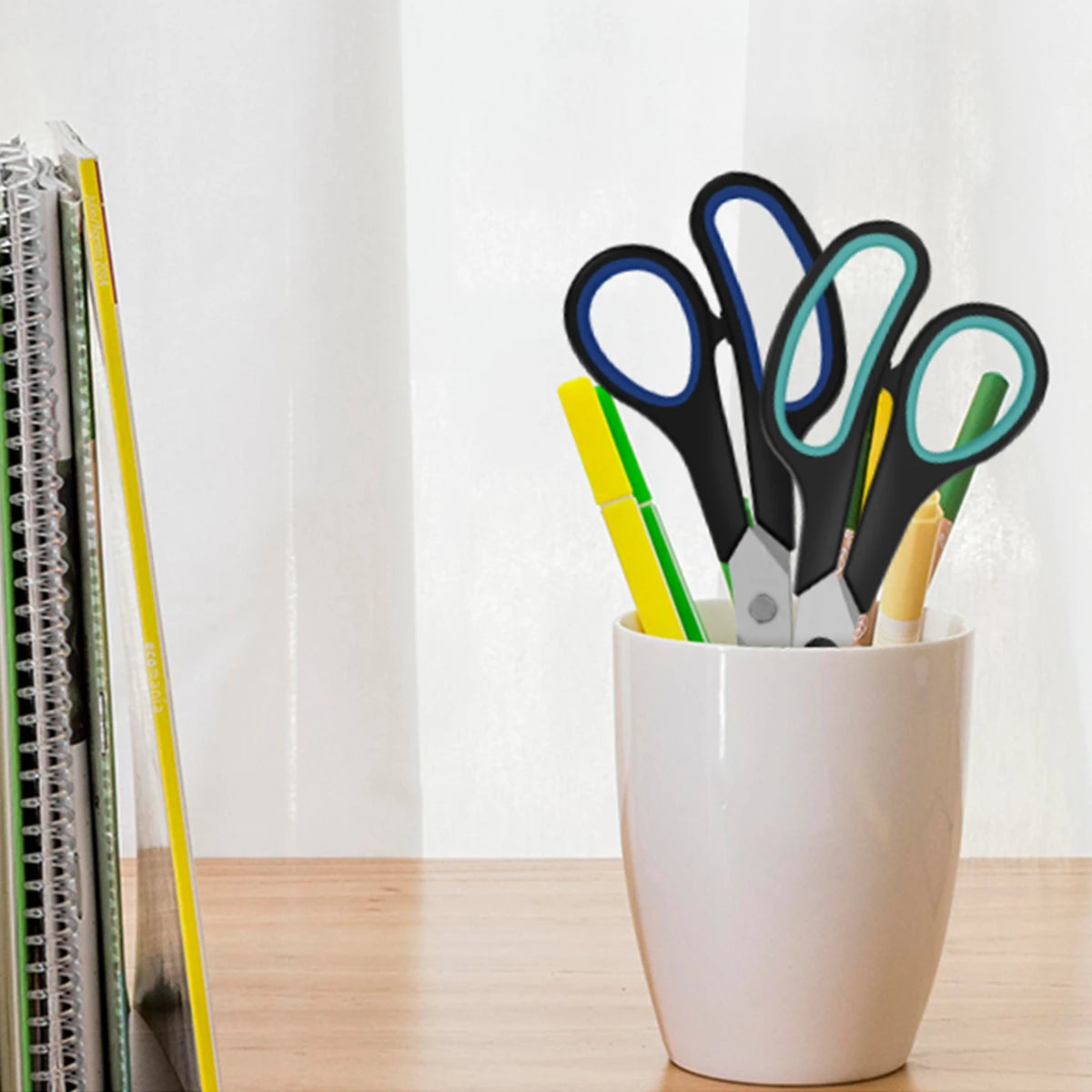 A collection of black and colored scissors with soft-grip handles displayed in a white pot.