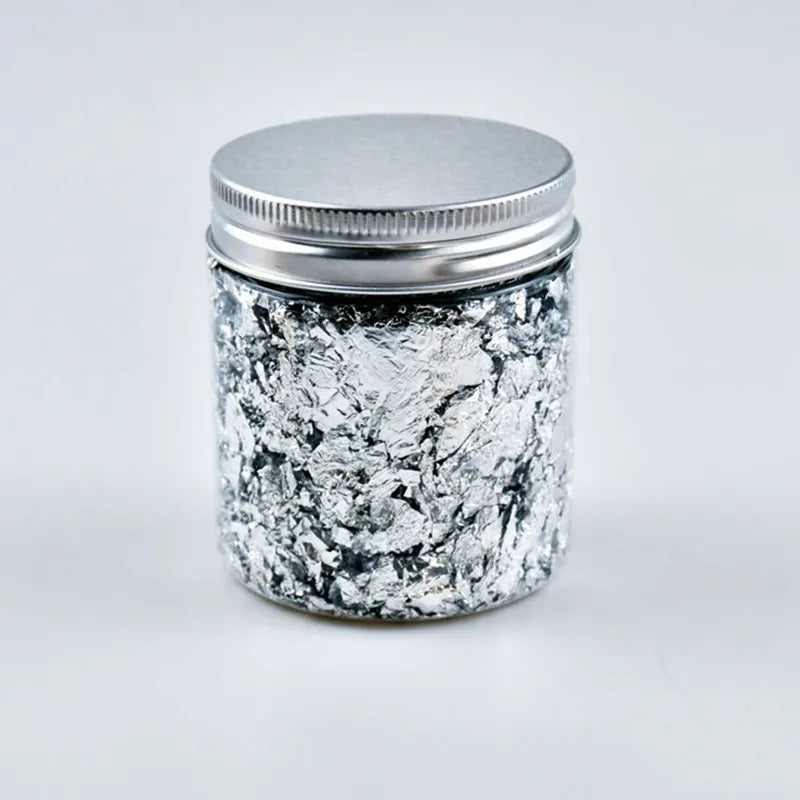 A glass jar with a silver lid filled with metallic foil flakes for crafting