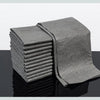 A stack of gray reusable microfiber cleaning cloths lying on a reflective surface.