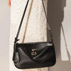 A black leather tote bag with a strap and metal buckle is shown against a light-colored textured background.