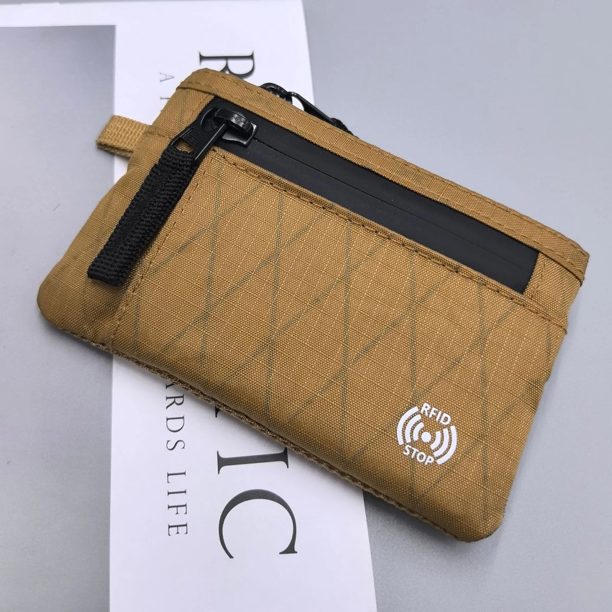 A tan RFID-blocking travel wallet with a black zipper and carabiner clip shown against a white background.