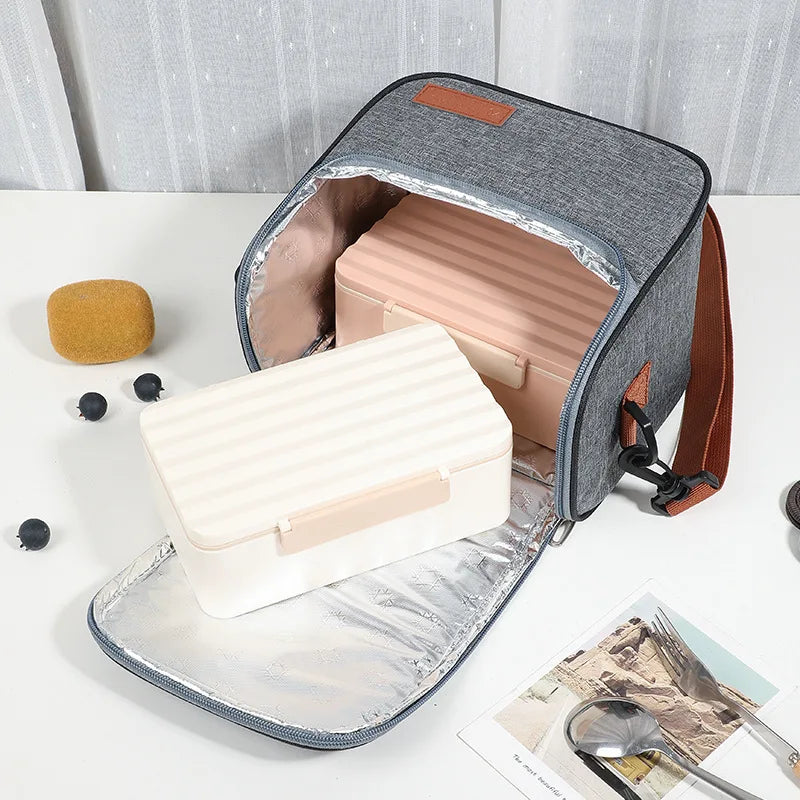 A gray insulated lunch bag with a pink interior and brown strap is shown open, displaying a white insulated food container.