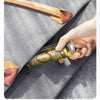 A hand holds a gold-colored electric razor with a leather handle against a gray fabric background.