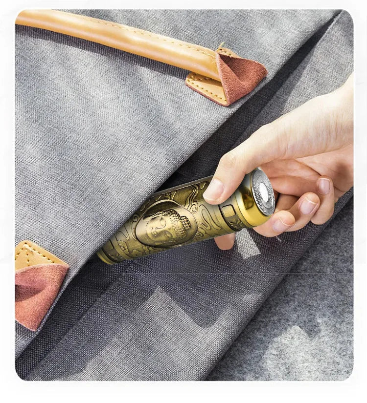A hand holds a gold-colored electric razor with a leather handle against a gray fabric background.