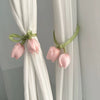 A set of pink tulip flower straps used as decorative tie backs on white curtains.