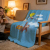 A light blue throw blanket featuring a cartoon character holding a yellow kite against a white cloudy background.