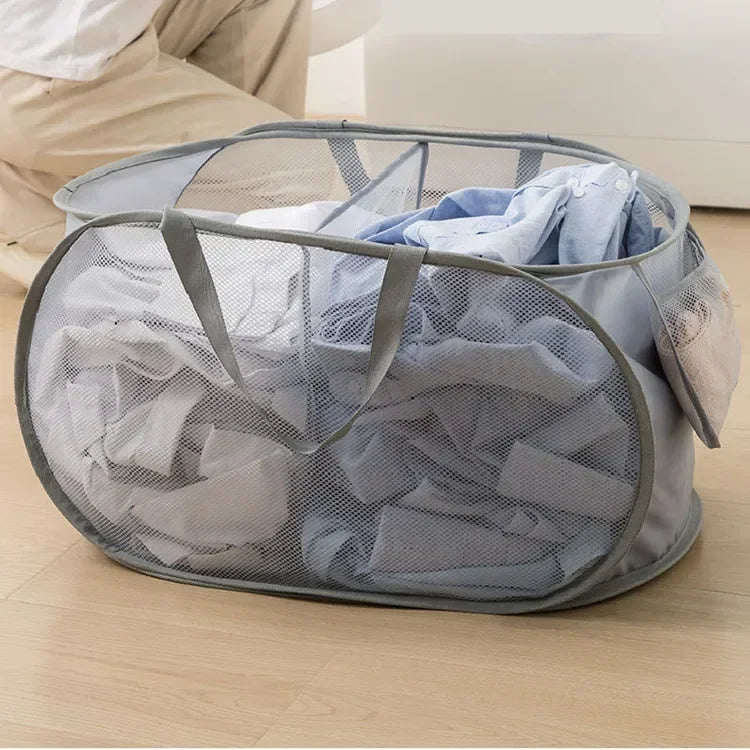 A gray folding mesh laundry basket with handles filled with folded blue and white clothing.