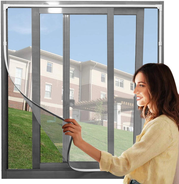 A woman is holding a magnetic mesh mosquito screen open in a sliding glass door, showing a residential building outside.