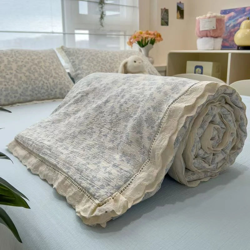 A rolled floral washed cotton gauze summer quilt with frayed edges resting on a light blue surface.