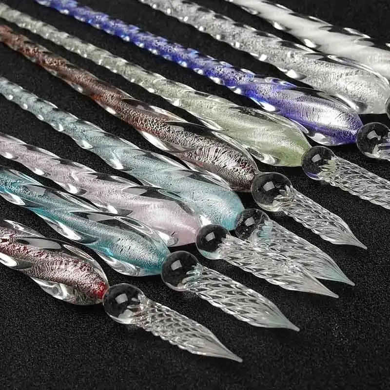 Colección de plumas de inmersión de vidrio cristal con tinta dorada, dispuestas en diagonal sobre una superficie oscura.