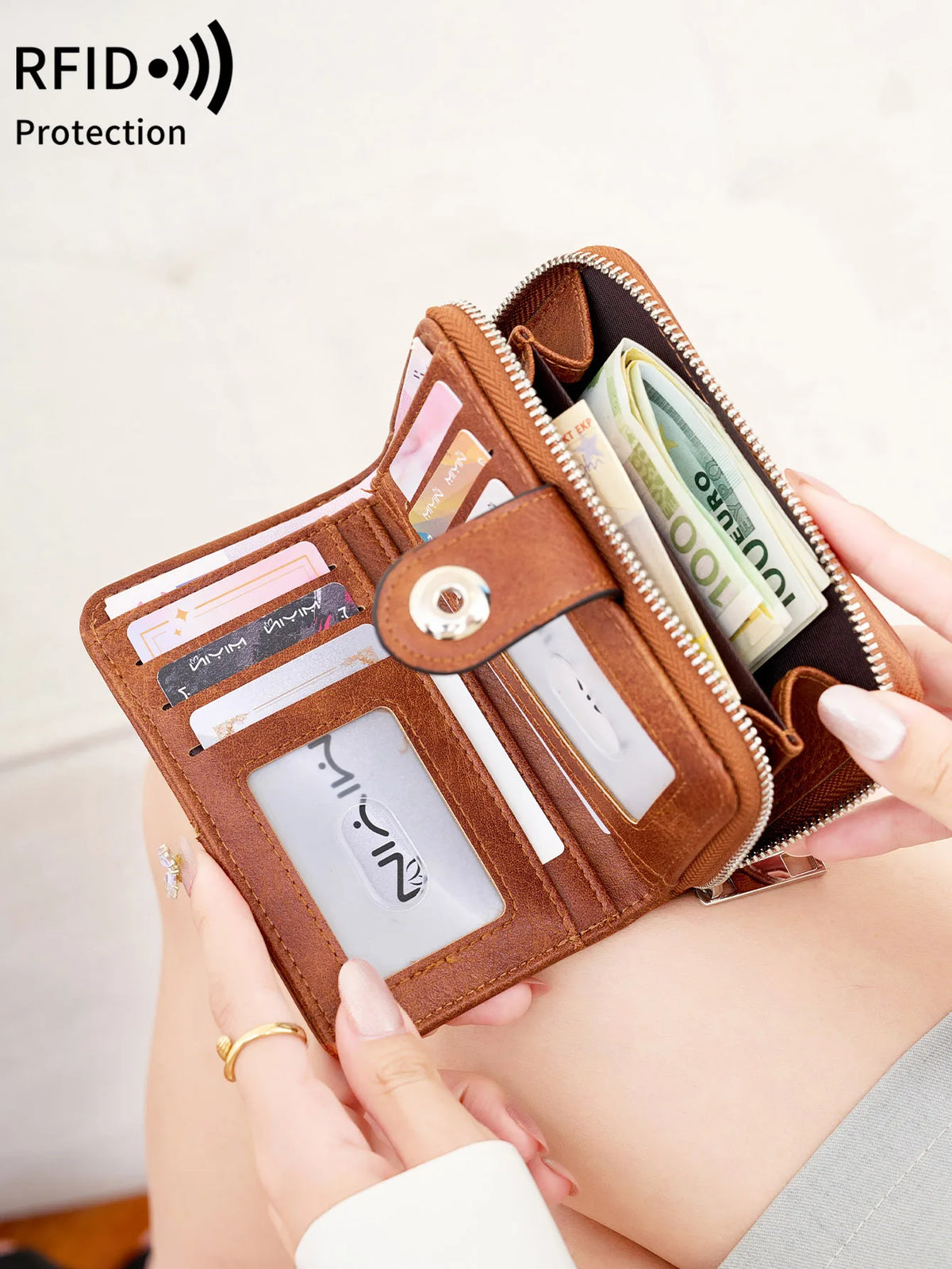 A brown vintage RFID blocking short wallet with a zipper closure is shown being held by a hand.