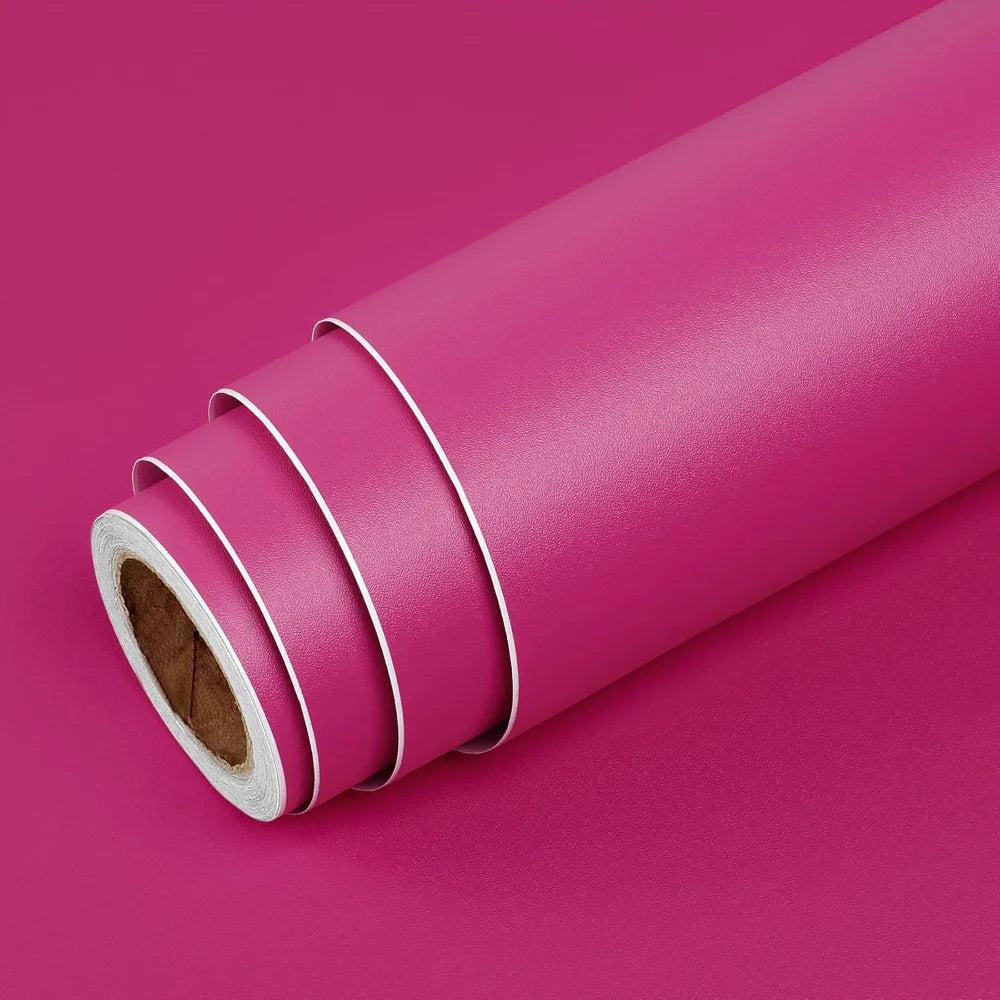 A roll of pink self-adhesive peel-and-stick wallpaper lying on a magenta surface.