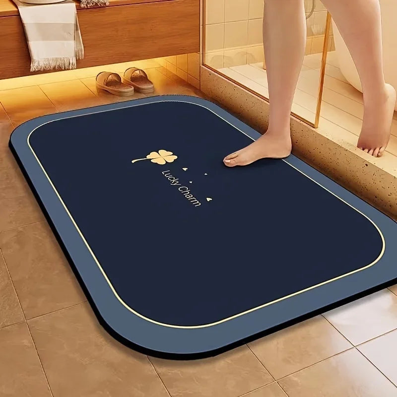 A dark blue diatomite bath mat with a gold trim is placed on a tiled floor next to a bathtub.
