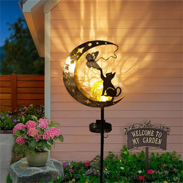 A decorative cat moon solar garden light mounted on a stake, casting shadows on a wooden wall.