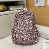 A pink leopard print nylon backpack with multiple pockets resting on a light-colored surface.