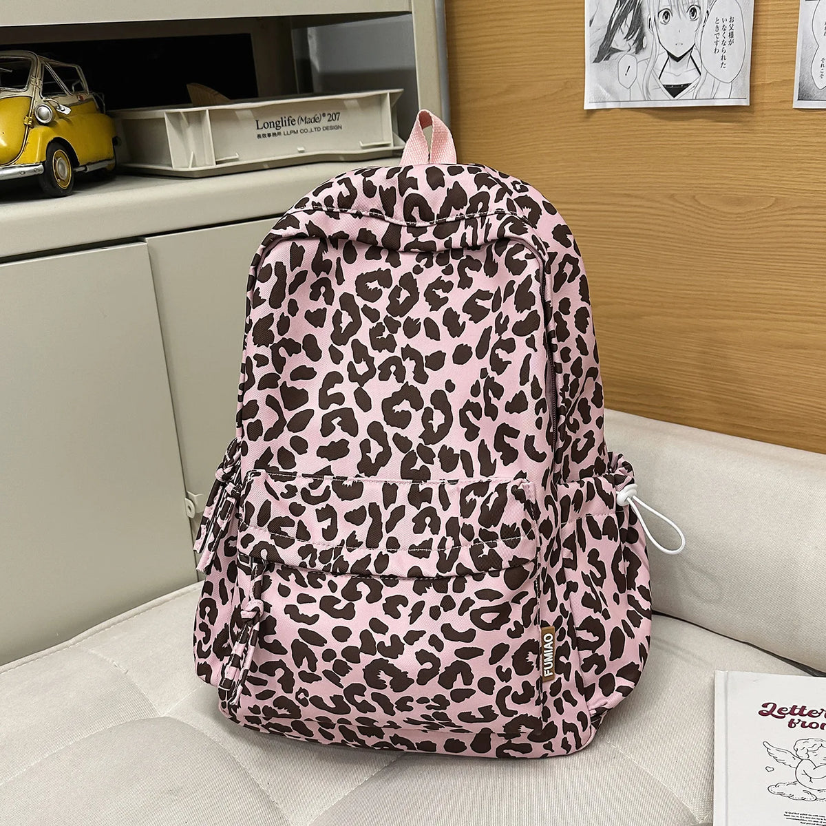 A pink leopard print nylon backpack with multiple pockets resting on a light-colored surface.