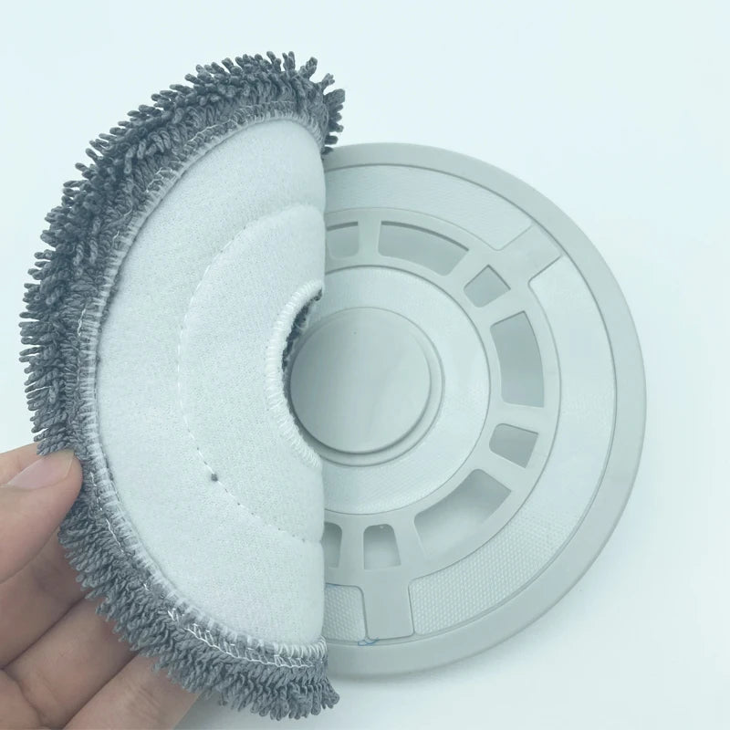 A hand holds a replacement part kit for a Dreame robot vacuum cleaner, showing a cleaning brush and a circular disc.