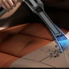 A handheld vacuum cleaner is cleaning dust from a car's leather interior surface.
