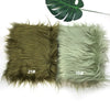 Two pieces of soft faux fur fabric in olive green and pale mint green, labeled 21# and 19#, with a monstera leaf in the backg