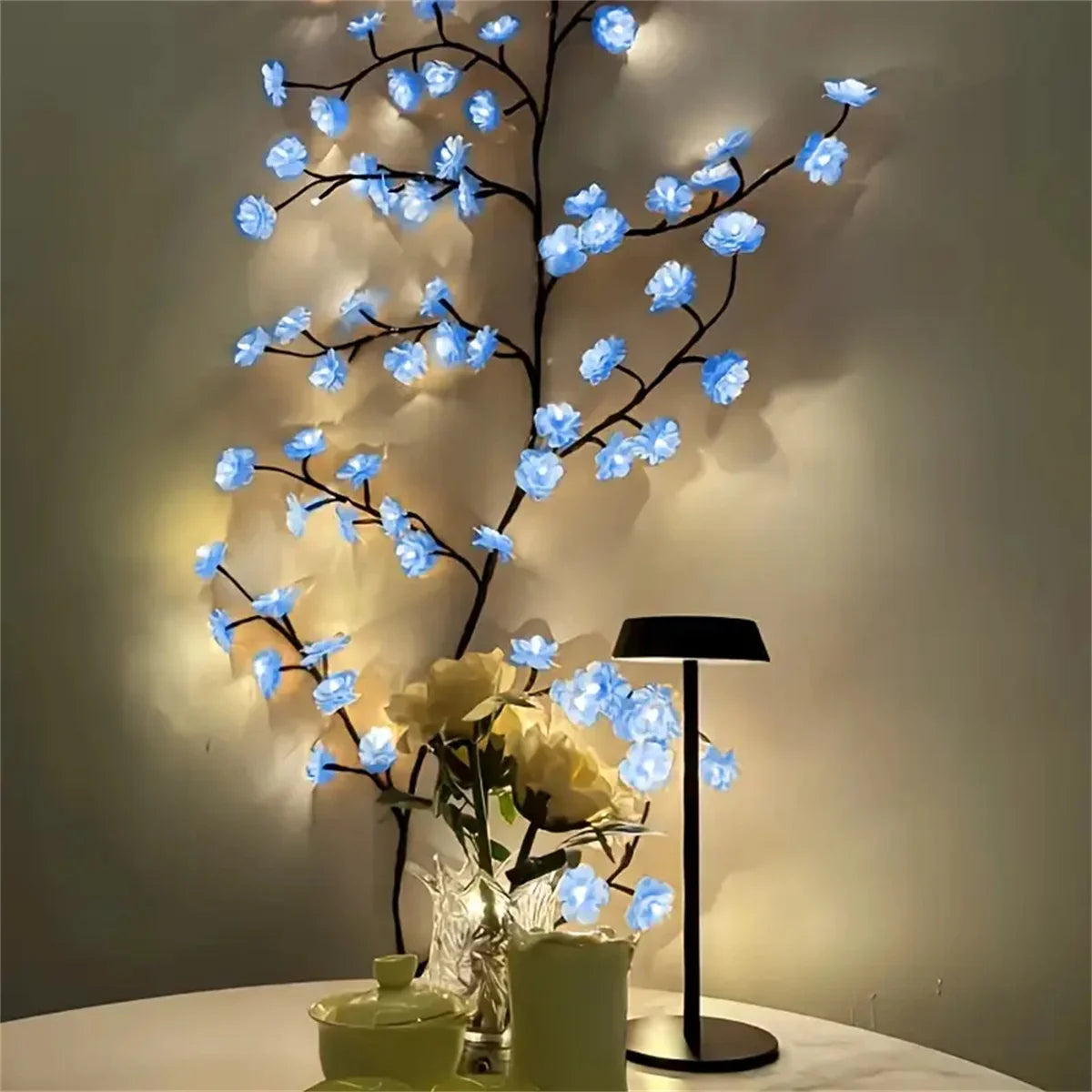 A decorative light display featuring blue cherry blossom LED lights illuminating a branch and white flowers.