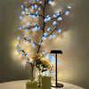 A decorative light display featuring blue cherry blossom LED lights illuminating a branch and white flowers.
