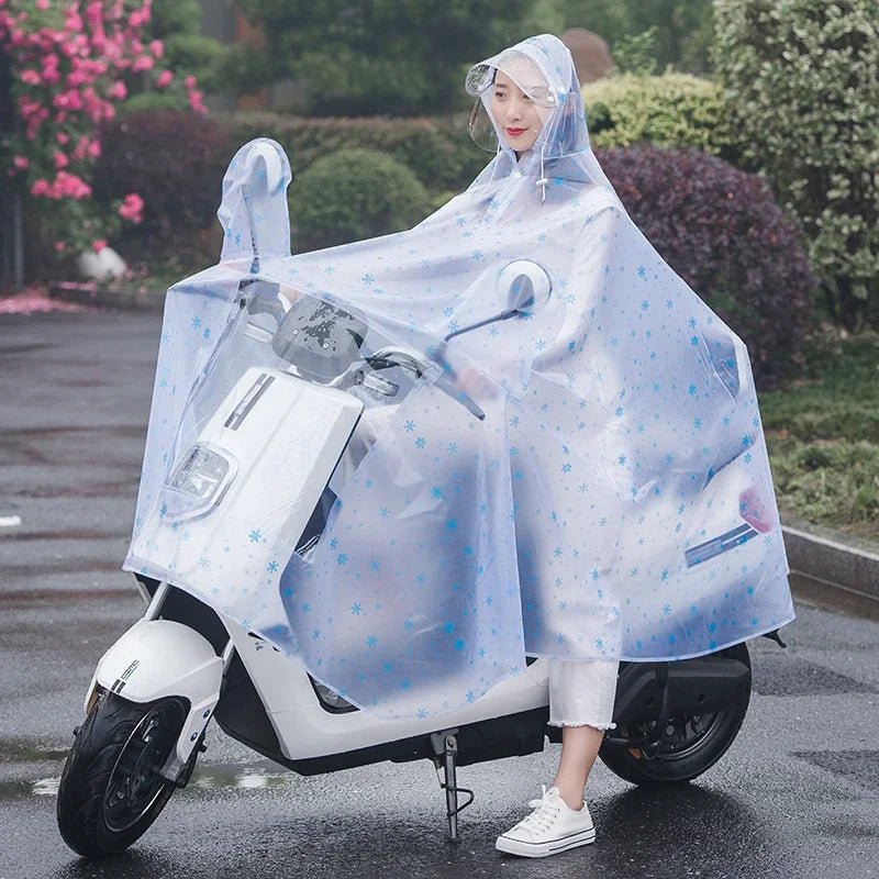 A person wearing a transparent waterproof motorcycle rain poncho with a hood is sitting on a white scooter on a wet road.