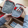 A hand opens a red travel medicine organizer bag, revealing compartments for various medications.