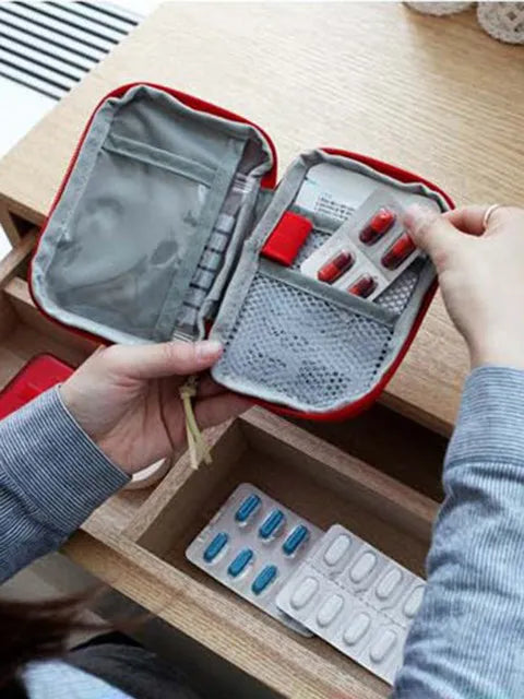 A hand opens a red travel medicine organizer bag, revealing compartments for various medications.